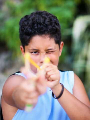 A boy thinking about releasing a slingshot at the camera.