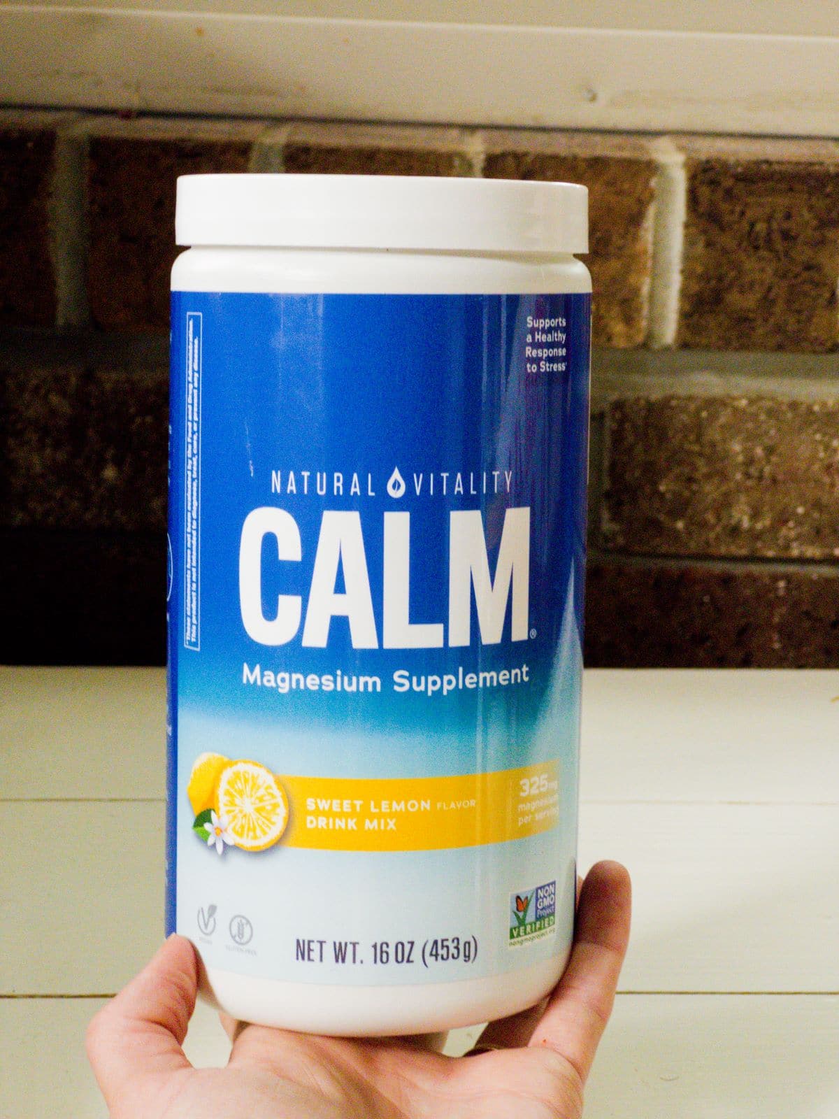 The author's hand holding the container of Magnesium Calm powder, lemon flavor.