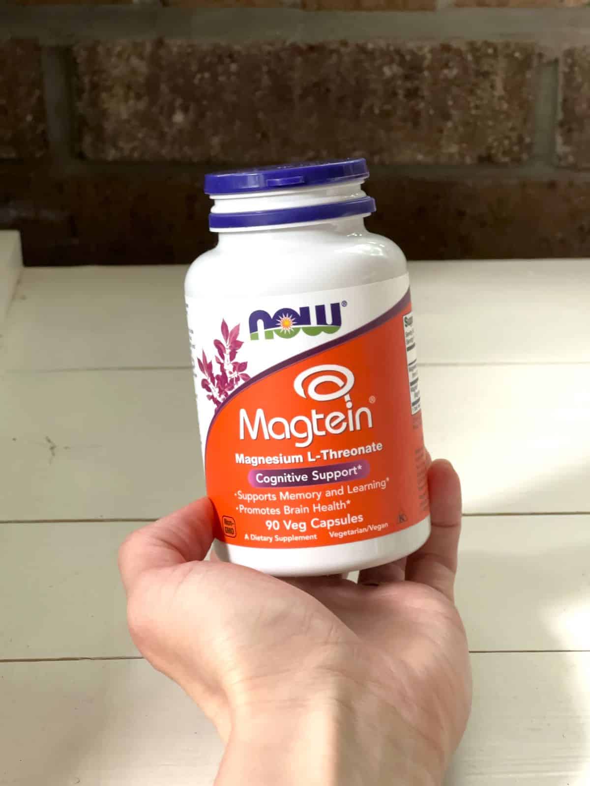 The blog author's hand holding a bottle of NOW Magtein Magnesium L-Threonate.
