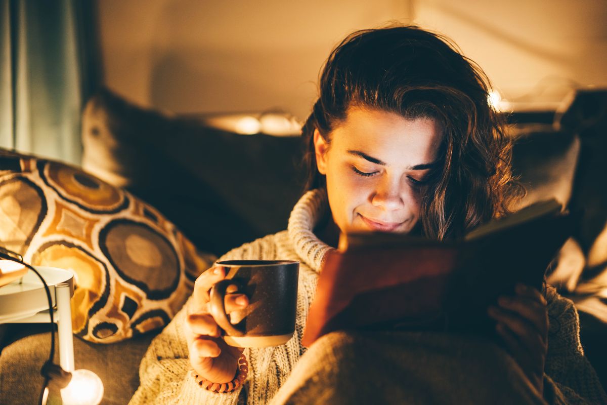 Woman with ADHD relaxing before bed, reading a book and drinking tea as part of a calming bedtime routine.