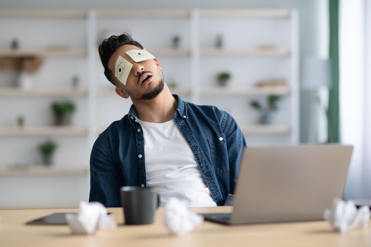 Tired man struggling with sleep deprivation at work after staying up too late from revenge bedtime procrastination, showing the impact on focus and ADHD symptoms.