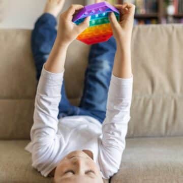 A kid on a sofa with his feet in the air holding a rainbow toy gift.