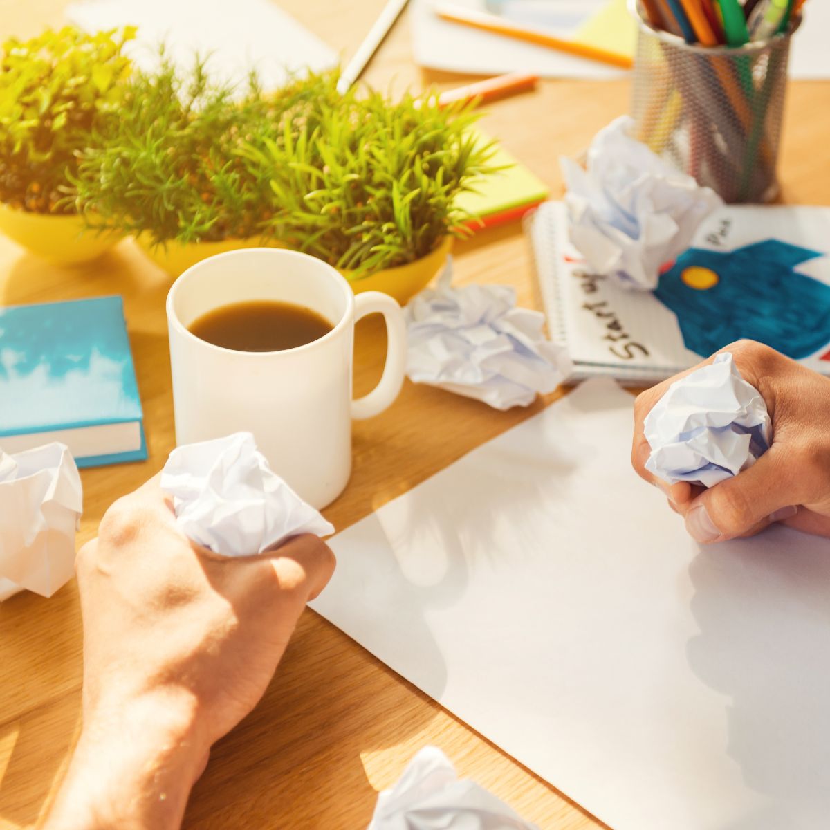 A person sitting at a cluttered desk filled with crumpled papers, a notebook, pens, and a cup of coffee, squeezing paper in frustration while struggling to start or finish a task. The scene reflects overwhelm and difficulty sticking to projects with ADHD.