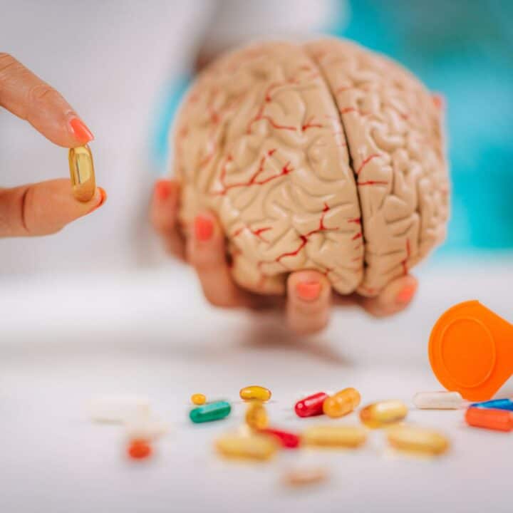 A person's hands holding a fake brain and a vitamin with the text "MTHFR & Vitamins for ADHD."