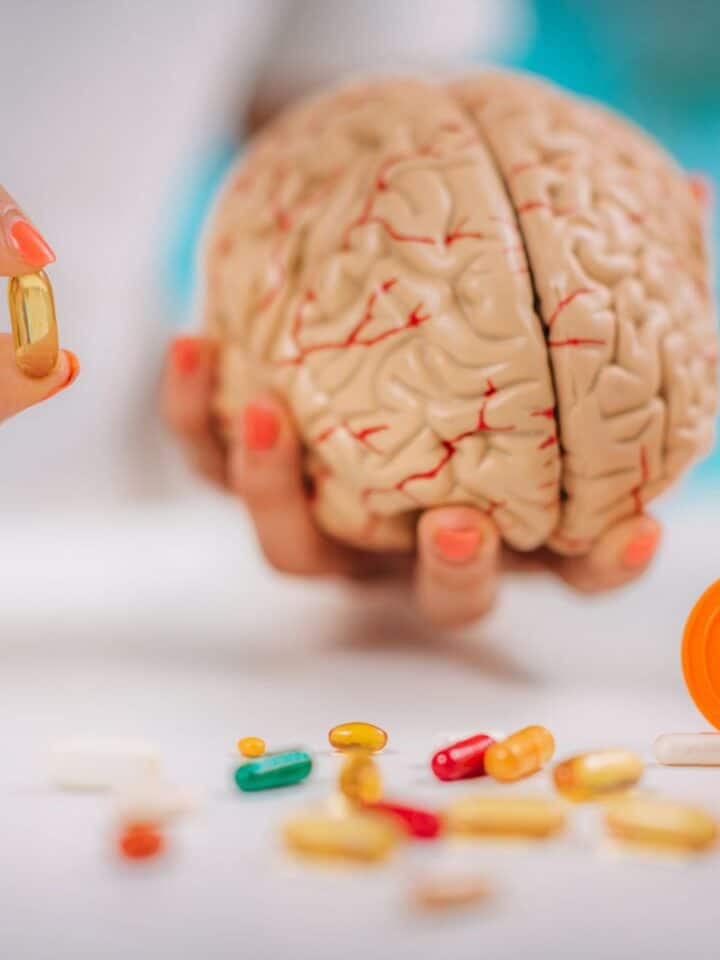 A person's hands holding a fake brain and vitamins nearby.