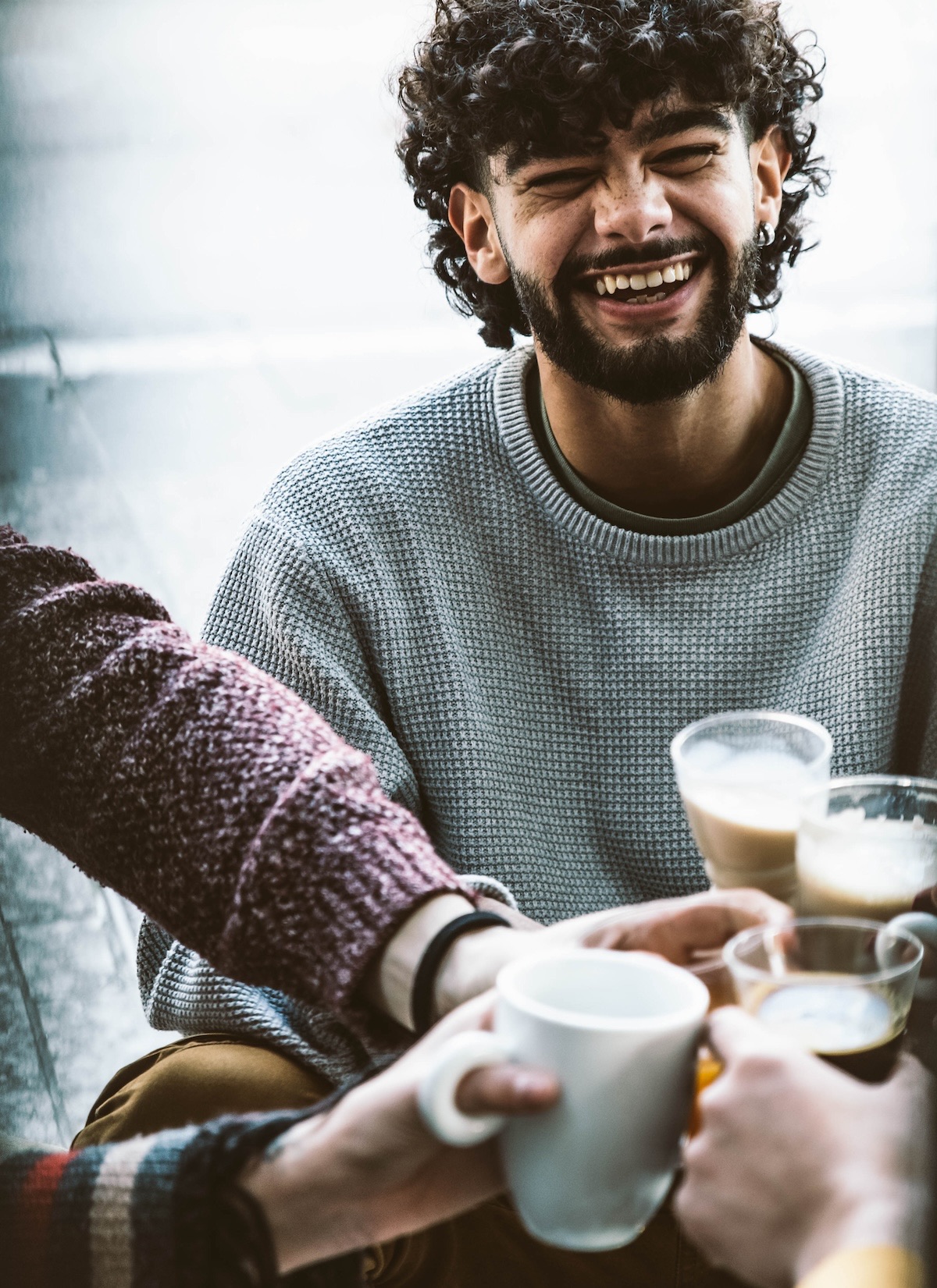 A man laughing at a coffee shop with friends.