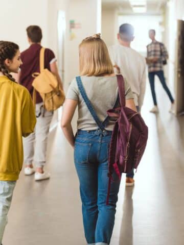 Several kids teens walking in a high school hall.